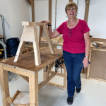 A smiling woman standing next to a saw horse she has constructed